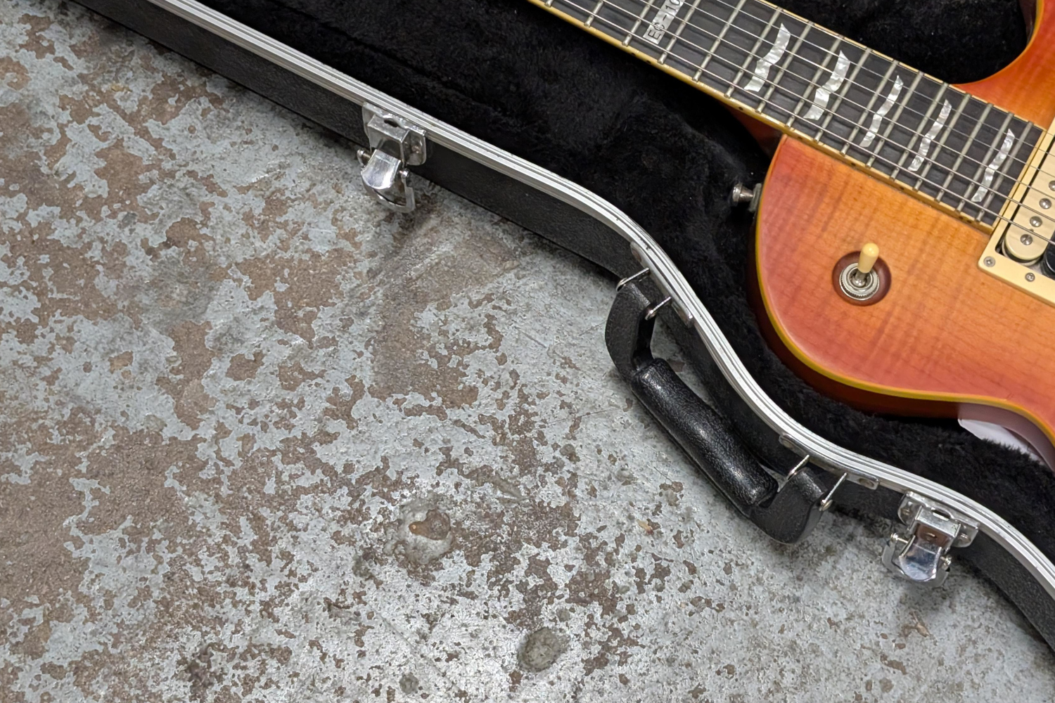 Electric guitar in a case on a rough concrete floor.